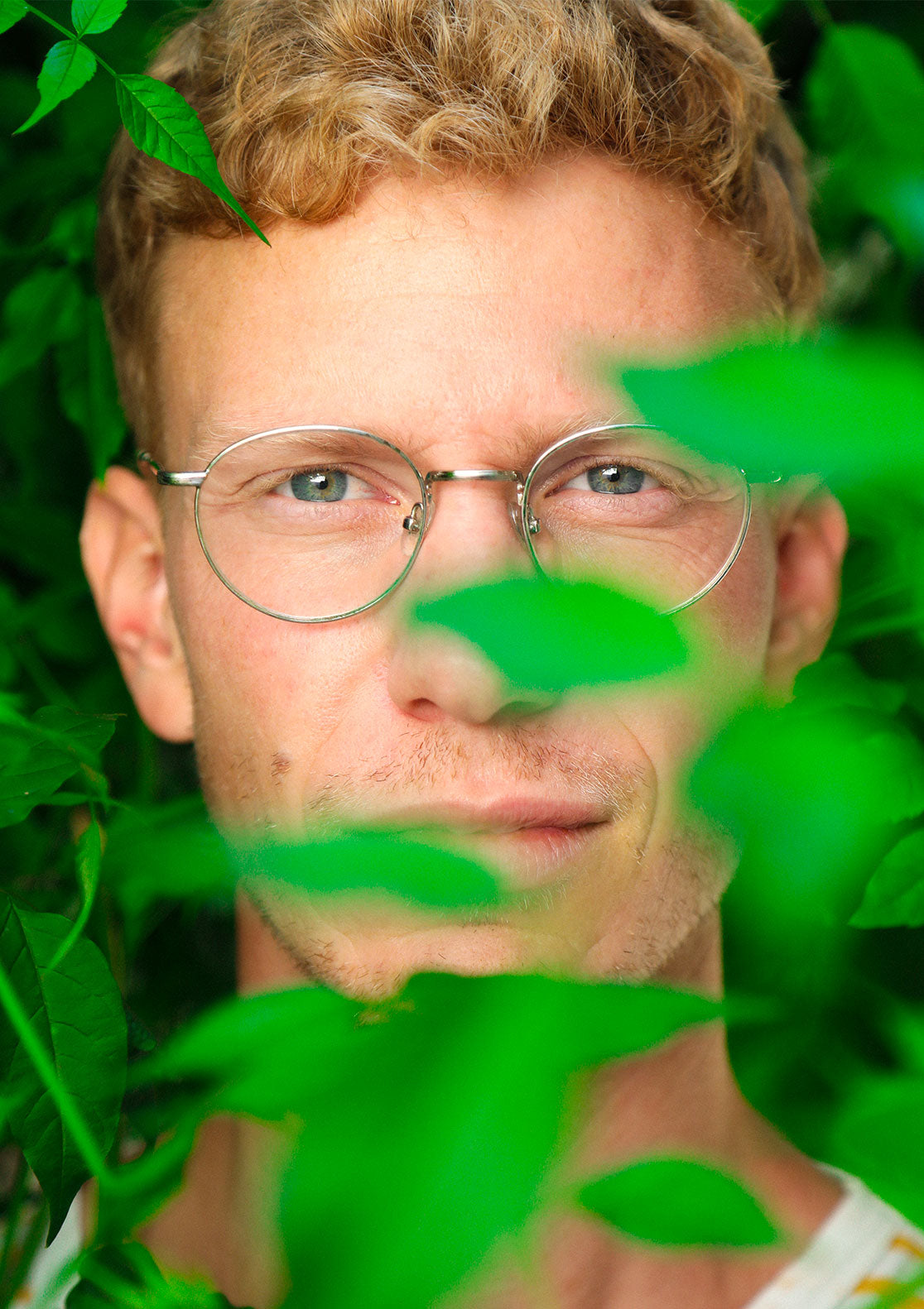 Homme aux cheveux blonds avec lunettes, feuilles vertes, regard sérieux