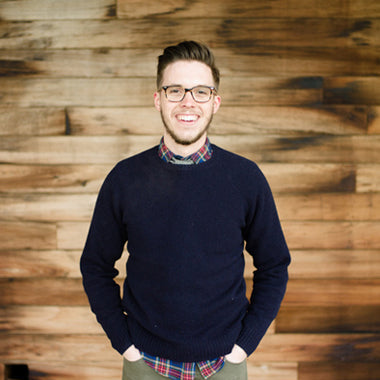 Homme souriant, lunettes, chemise à carreaux, pull noir, mur en bois