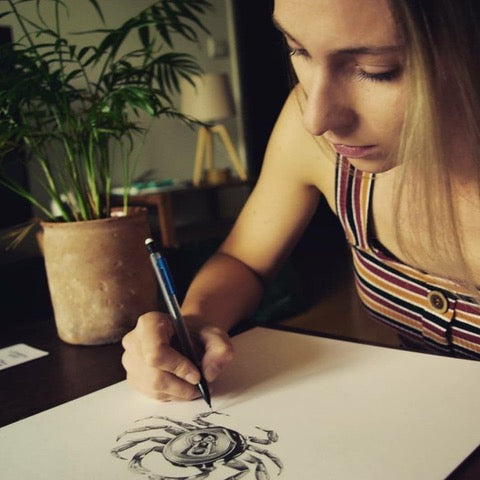 Femme dessinant un crabe sur papier, plante en pot, lampe de bureau